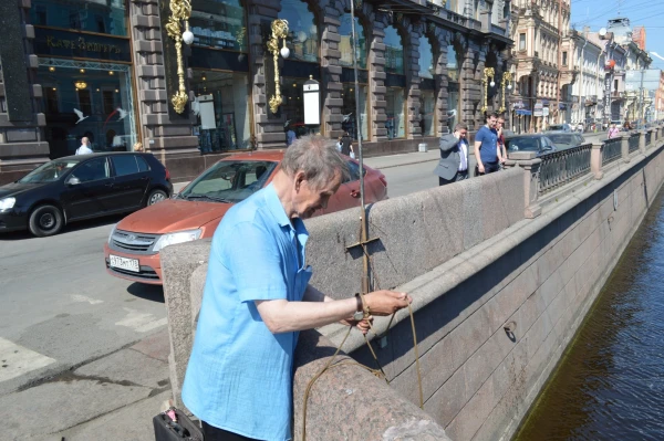 Дед пристроил магнит на веревкку и вылавливает денежки из Мойки